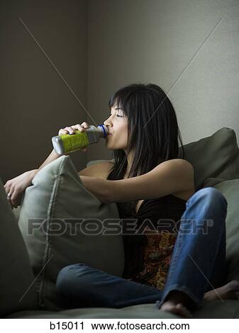 Woman drinking beverage while sitting on sofa View Large Photo Image Stock Image - Woman drinking beverage while sitting on sofa. Fotosearch