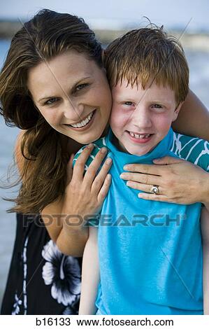 Stock Image - Woman embracing boy wrapped in towel outdoors smiling. Fotosearch