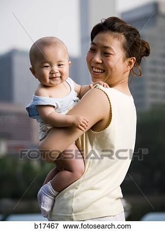 Stock Photo - Woman holding baby outdoors smiling. Fotosearch