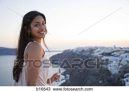 Stock Image - Woman holding champagne flute outdoors smiling. Fotosearch