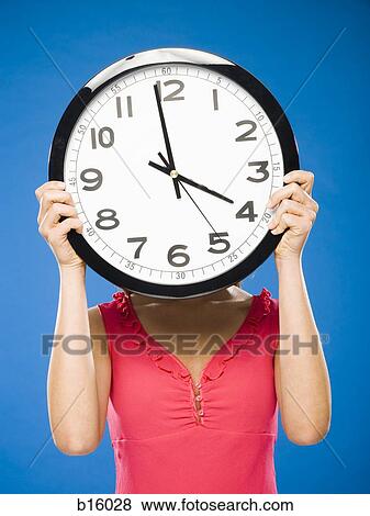 Stock Photo - Woman holding clock over face at one minute to four. Fotosearch