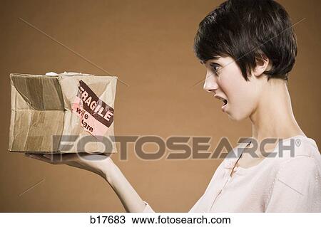 Stock Image - Woman holding crushed cardboard box with fragile label. Fotosearch