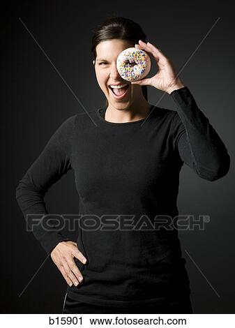 Stock Image - Woman holding donut up to eye and smiling. Fotosearch
