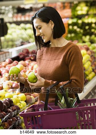 Woman holding green apples at grocery store with shopping basket View Large Photo Image Stock Photo - Woman holding green apples at grocery store with shopping basket. Fotosearch