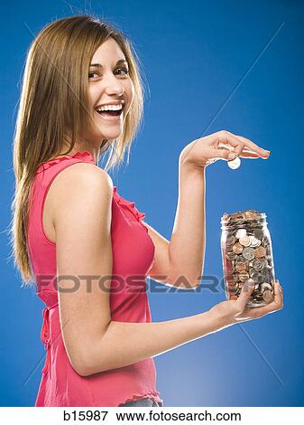 Stock Photo - Woman holding jar filled with coins smiling. Fotosearch