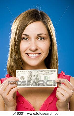 Stock Image - Woman holding one hundred American dollar bill smiling. Fotosearch