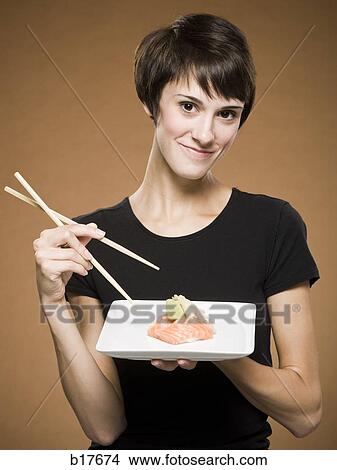 Woman holding sushi plate with chopsticks smiling View Large Photo Image Picture - Woman holding sushi plate with chopsticks smiling. Fotosearch