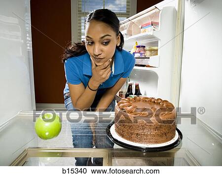 Woman in refrigerator with apple looking at chocolate cake View Large Photo Image Stock Image - Woman in refrigerator with apple looking at chocolate cake. Fotosearch