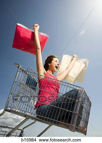 Woman in shopping cart outdoors with shopping bags smiling View Large Photo Image Picture - Woman in shopping cart outdoors with shopping bags smiling. Fotosearch