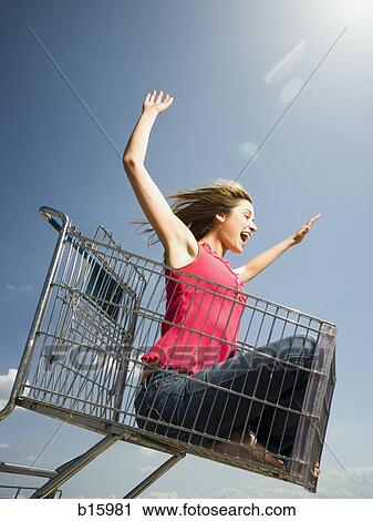 Woman in shopping cart outdoors with arms up smiling View Large Photo Image Stock Image - Woman in shopping cart outdoors with arms up smiling. Fotosearch