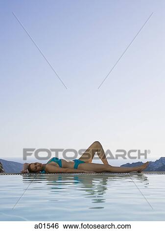 Woman in swimsuit lying down beside infinity pool outdoors View Large Photo Image Stock Photograph - Woman in swimsuit lying down beside infinity pool outdoors. Fotosearch