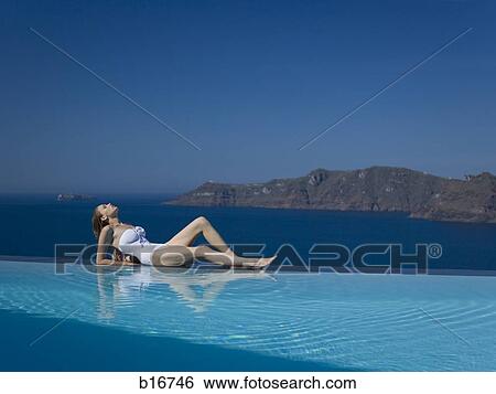 Woman in swimsuit reclining at edge of infinity pool outdoors View Large Photo Image Stock Photograph - Woman in swimsuit reclining at edge of infinity pool outdoors. Fotosearch