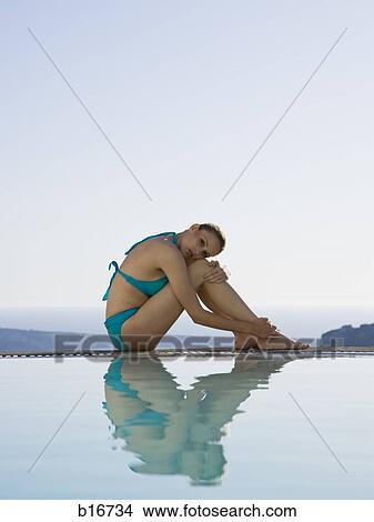 Woman in swimsuit sitting at edge of infinity pool outdoors View Large Photo Image Picture - Woman in swimsuit sitting at edge of infinity pool outdoors. Fotosearch