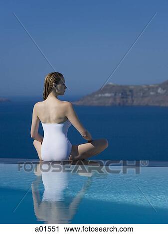 Woman in swimsuit sitting cross legged by infinity pool outdoors View Large Photo Image Stock Image - Woman in swimsuit sitting cross legged by infinity pool outdoors. Fotosearch