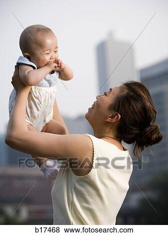 Woman lifting baby outdoors and smiling View Large Photo Image Stock Photo - Woman lifting baby outdoors and smiling. Fotosearch