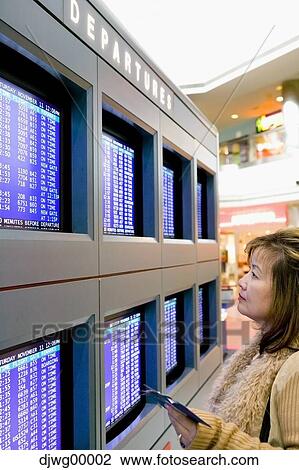 Stock Image - Woman looking at departures monitors at airport. Fotosearch