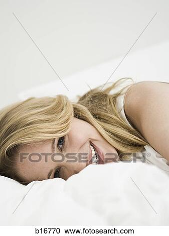 Stock Image - Woman lying down in bed smiling. Fotosearch