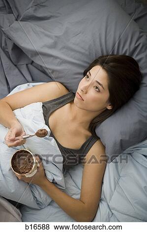 Woman lying in bed eating chocolate ice cream View Large Photo Image Stock Photo - Woman lying in bed eating chocolate ice cream. Fotosearch