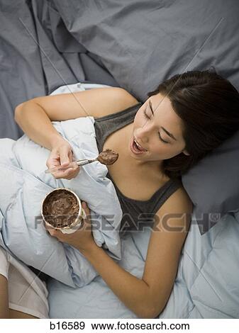 Woman lying in bed eating chocolate ice cream View Large Photo Image Stock Photo - Woman lying in bed eating chocolate ice cream. Fotosearch