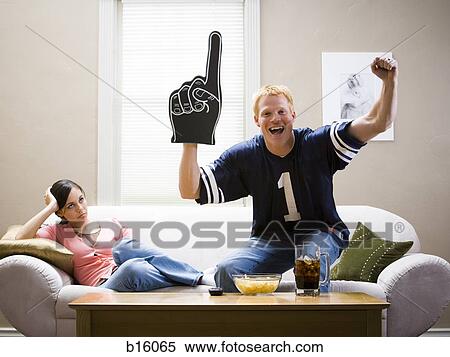 Woman on sofa and man in football jersey standing and cheering View Large Photo Image Stock Photography - Woman on sofa and man in football jersey standing and cheering. Fotosearch