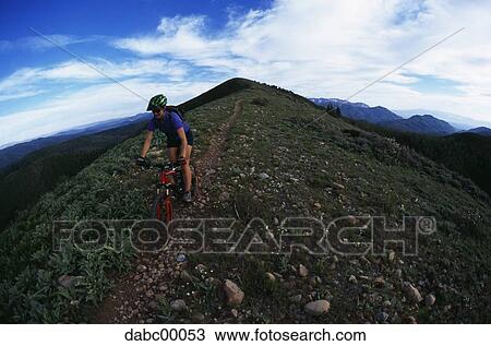 Stock Image - Woman riding mountain bike on hill with blue sky. Fotosearch
