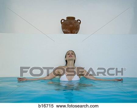 Stock Photography - Woman sitting and leaning against wall in pool under urn. Fotosearch