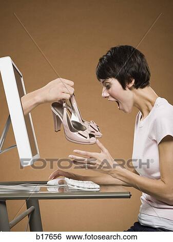 Stock Photograph - Woman sitting at computer with hand emerging from monitor holding pumps. Fotosearch