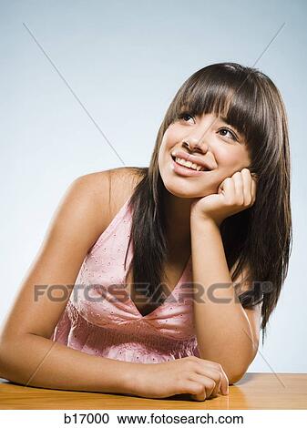 Woman sitting at desk leaning on hand looking up smiling View Large Photo Image Stock Image - Woman sitting at desk leaning on hand looking up smiling. Fotosearch