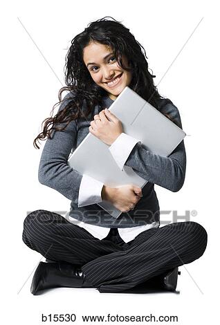 Stock Image - Woman sitting cross legged hugging laptop. Fotosearch