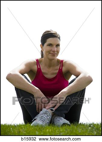 Stock Image - Woman sitting cross legged on grass outdoors smiling. Fotosearch