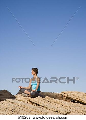 Woman sitting cross legged on rock outdoors doing yoga View Large Photo Image Stock Photo - Woman sitting cross legged on rock outdoors doing yoga. Fotosearch