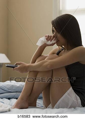Woman sitting on bed with television remote and tissue View Large Photo Image Stock Image - Woman sitting on bed with television remote and tissue. Fotosearch