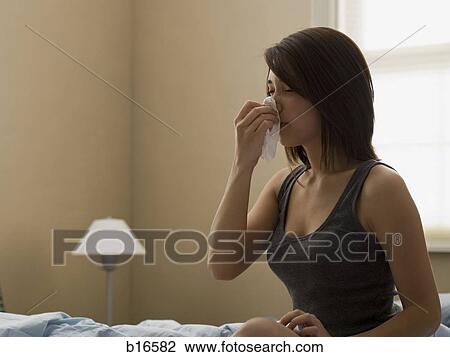 Woman sitting on bed with tissue to nose View Large Photo Image Stock Image - Woman sitting on bed with tissue to nose. Fotosearch