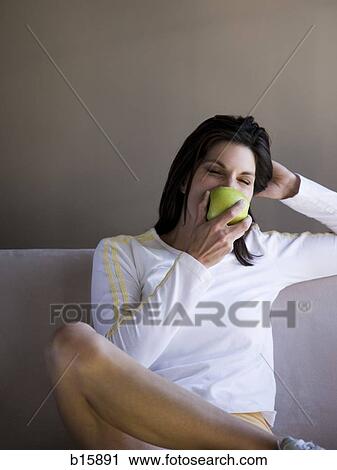 Woman sitting on sofa eating green apple View Large Photo Image Stock Image - Woman sitting on sofa eating green apple. Fotosearch