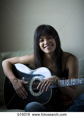 Woman sitting on sofa holding guitar smiling View Large Photo Image Stock Photo - Woman sitting on sofa holding guitar smiling. Fotosearch