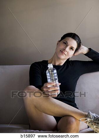 Woman sitting on sofa with bottled water smiling View Large Photo Image Stock Photo - Woman sitting on sofa with bottled water smiling. Fotosearch