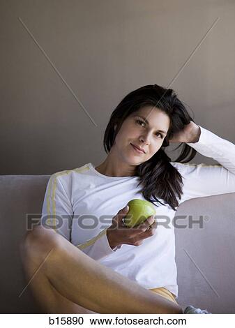 Woman sitting on sofa with green apple View Large Photo Image Stock Image - Woman sitting on sofa with green apple. Fotosearch