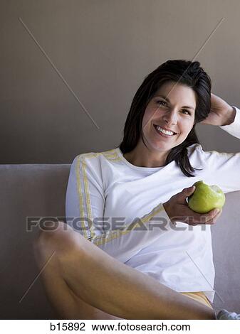 Woman sitting on sofa with green apple smiling View Large Photo Image Stock Image - Woman sitting on sofa with green apple smiling. Fotosearch