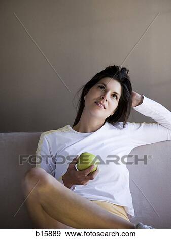 Woman sitting on sofa with green apple View Large Photo Image Stock Photo - Woman sitting on sofa with green apple. Fotosearch