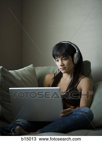 Woman sitting on sofa with laptop and headphones View Large Photo Image Stock Image - Woman sitting on sofa with laptop and headphones. Fotosearch