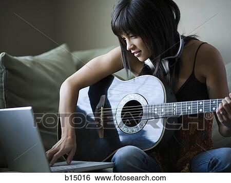 Woman sitting on sofa with laptop and guitar View Large Photo Image Stock Photograph - Woman sitting on sofa with laptop and guitar. Fotosearch