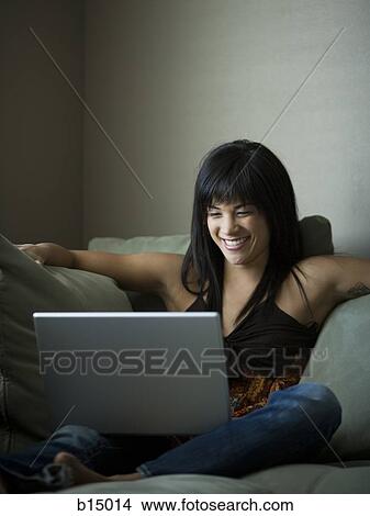 Woman sitting on sofa with laptop smiling View Large Photo Image Picture - Woman sitting on sofa with laptop smiling. Fotosearch