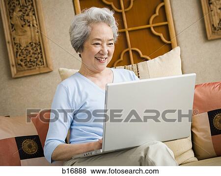 Woman sitting on sofa with laptop smiling View Large Photo Image Stock Photo - Woman sitting on sofa with laptop smiling. Fotosearch