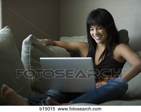Woman sitting on sofa with laptop smiling View Large Photo Image Stock Photography - Woman sitting on sofa with laptop smiling. Fotosearch