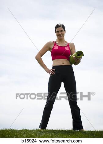 Woman standing on grass outdoors smiling with rolled yoga mat View Large Photo Image Picture - Woman standing on grass outdoors smiling with rolled yoga mat. Fotosearch