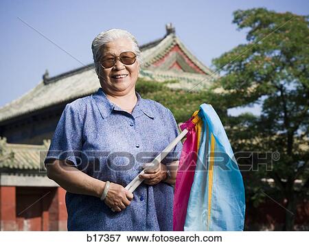 Stock Photo - Woman standing outdoors with fabric on sticks with pagoda in background smiling. Fotosearch