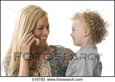 Stock Image - Woman talking on cell phone smiling at boy. Fotosearch
