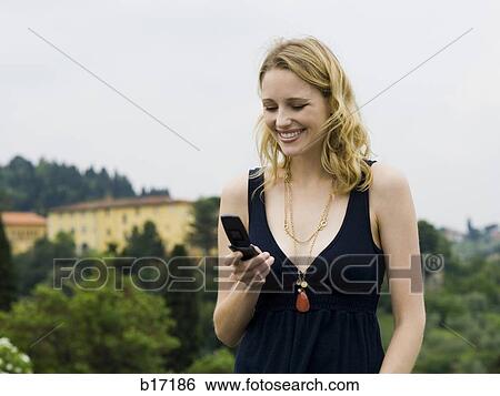 Stock Photograph - Woman with cell phone outdoors smiling. Fotosearch