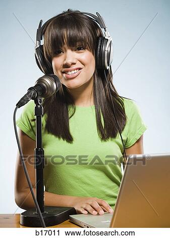 Stock Image - Woman with headphones and laptop singing into microphone. Fotosearch