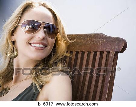 Woman with sunglasses sitting in wooden chair outdoors smiling View Large Photo Image Stock Photo - Woman with sunglasses sitting in wooden chair outdoors smiling. Fotosearch